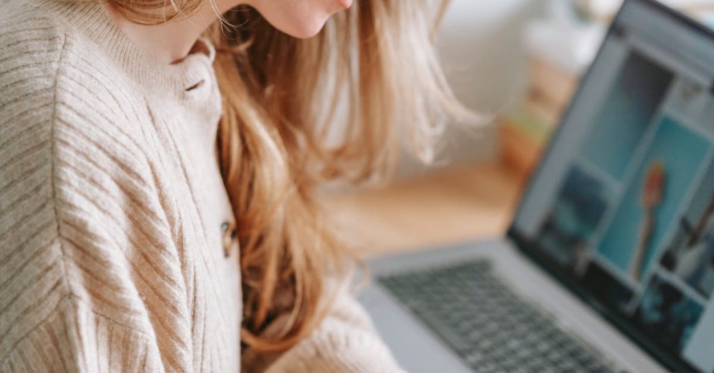 Side view of crop focused female taking notes in planner at table with netbook on blurred background